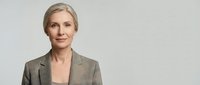 Mature woman with short blonde hair wearing a beige blazer over a neutral top, isolated on white background for corporate and professional design use.