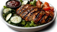 Grilled chicken breast with grill marks served on fresh green salad with cucumber slices, cherry tomatoes and dark sauce in white ceramic bowl.