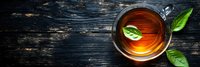 Fresh hot tea with green leaves in glass cup on dark rustic wooden background, top view panoramic banner composition with copy space.