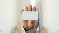 Male professional in light blue shirt holding blank white business card toward camera, suitable for corporate branding and business communication projects.