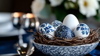 Decorative Easter eggs with blue floral pattern in porcelain bowl with nest. White and navy traditional painted eggs create elegant holiday composition.
