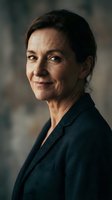 Middle-aged woman with dark hair wearing dark blazer, smiling at camera against blurred background. Corporate professional portrait for business, leadership, and corporate communications.