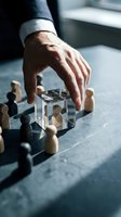 Businessman hand protecting wooden figure in glass cube surrounded by diverse team members representing leadership and employee protection concept.