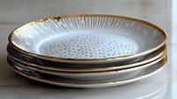 Stack of elegant white porcelain plates with gold rim and delicate polka dot pattern, arranged on light surface. Modern dinnerware for luxury table setting.