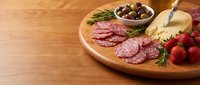 Gourmet charcuterie board with sliced salami, aged cheese, mixed olives, fresh strawberries and herbs on wooden platter for entertaining and appetizers.