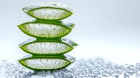 Fresh aloe vera leaves stacked with clear gel visible through translucent green skin, surrounded by water drops on white surface, natural skincare concept.