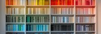 Colorful rainbow bookshelf with books arranged by color spectrum from red to purple creating ombre effect. Modern library interior with organized color-coded book collection.