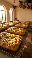 Fresh baked artisan bread loaves cooling on racks in rustic Mediterranean kitchen with arched windows and copper pots hanging from ceiling beams.