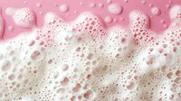 White soap foam bubbles on pink background with water drops and frothy texture creating abstract pattern of various sized spherical shapes and suds.
