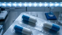 Blue and white pharmaceutical capsules in blister pack on laboratory table with medical equipment and LED lighting in modern research facility.