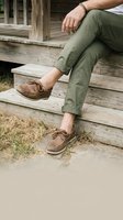 Man in olive green pants and brown leather shoes sitting on wooden steps outdoors in casual relaxed pose for lifestyle and fashion concepts.