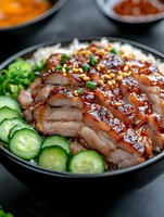 Sliced glazed roasted duck breast with teriyaki sauce served in black bowl with rice, fresh cucumber and green onions. Asian cuisine close up view.