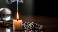 Burning candle with smoke, pentagram symbol, crystal ball and dried herbs create mystical witchcraft scene for spiritual practices and occult rituals.