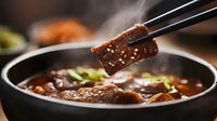 Juicy beef slice held by chopsticks over steaming hot pot with savory broth, garnished with green onions and sesame seeds, dramatic lighting for food photography.