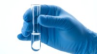 Gloved hand in blue latex glove holding a clear glass test tube with liquid, science research and medical laboratory concept.