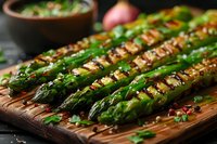 Grilled green asparagus spears on wooden cutting board garnished with sesame seeds, herbs and spices. Close up view of roasted vegetables for healthy meal.