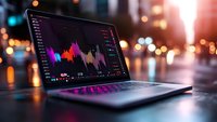 Laptop displaying colorful financial charts and trading data on screen with blurred city lights background for business analysis and investment decisions.