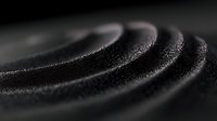 Macro shot of black sand arranged in concentric circular waves creating mesmerizing pattern with shallow depth of field and dramatic lighting effect.