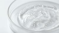 Transparent gel or serum swirling in a clear glass container, showing viscous liquid texture for skincare, cosmetics, and beauty product packaging design.