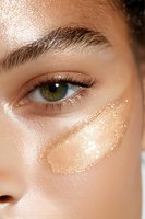 Close-up of green eye with glowing golden highlighter makeup on smooth skin, showing professional beauty cosmetics application and glitter details.