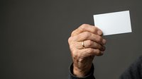 Mature male hand holding blank white card against neutral gray background for business messaging and corporate communication.