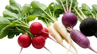 Fresh colorful radishes with green tops, including red, white, purple, and black varieties, arranged on a white background for healthy food concepts.