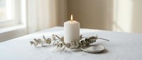 White pillar candle burning on ceramic plate with dried eucalyptus branches creating peaceful home decor atmosphere for relaxation and mindfulness.