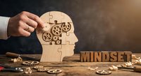 Business professional assembling wooden puzzle pieces forming human head with gears representing mindset development and cognitive growth strategies.