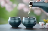 Traditional Japanese tea ceremony with ceramic teapot pouring green tea into handcrafted bowls surrounded by delicate cherry blossom flowers in serene setting.