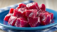 Fresh raw beef cubes cut for stew or cooking on blue plate. Premium red meat chunks ready for culinary preparation and gourmet recipes.