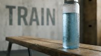 Water bottle with condensation sitting on wooden bench near train station sign, fitness and hydration concept.