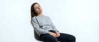 Young Caucasian woman in gray sweater relaxing in modern chair with eyes closed, expressing peace and mindfulness for wellness and mental health concepts.