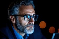 Mature businessman with gray beard wearing glasses in dramatic low key lighting against dark background with bokeh lights, professional corporate portrait.