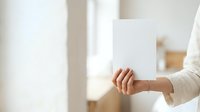 Woman holding blank white card in hand with neutral background, suitable for mockups, greeting cards, invitations, business promotions, and marketing materials.