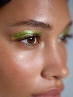 Close up of young Asian woman with bright green glitter eyeshadow and natural makeup look against neutral background, showcasing creative beauty trends.