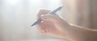 Close-up of female hand holding black pen in writing position against soft blurred background. Business professional ready to sign documents or take notes.