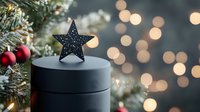 Festive black star decoration on round box against blurred Christmas lights and pine branches with red ornaments creates magical holiday atmosphere.
