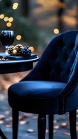 Elegant navy velvet chair with wine glass and pine cones on side table, warm bokeh lights creating cozy autumn atmosphere for luxury interior design.