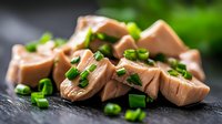 Fresh tuna steaks sliced and garnished with chopped green onions on dark slate surface. Raw fish preparation for sushi, sashimi or grilling recipes.