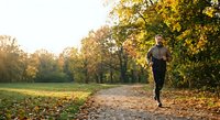 Young athletic man jogging on autumn park path surrounded by golden fall foliage during morning workout session for healthy lifestyle and fitness.