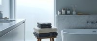 Modern minimalist bathroom interior with white marble surfaces, freestanding bathtub, wooden stool with folded towels and contemporary fixtures for luxury home design.
