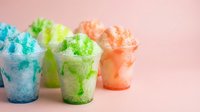 Colorful shaved ice cups with blue, green, and orange flavored snow cones on pink background, isolated ready for beverage and summer refreshment design use.