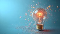 Glowing light bulb with sparkling particles dispersing against blue background, representing innovation, creativity, and bright ideas for business and technology concepts.