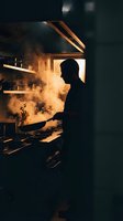 Professional chef silhouette cooking with dramatic flames and smoke in commercial kitchen. Culinary expertise and restaurant food preparation atmosphere.