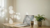 Laptop with coffee cup and potted plant on wooden desk near window with soft natural light and blurred background for workspace design.