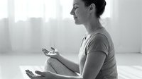 Woman in casual attire sitting cross-legged on floor in bright, minimalist space, holding smartphone, practicing mindfulness and meditation for wellness and mental health.