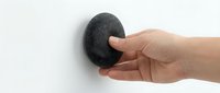 Close-up of a hand holding a dark gray pumice stone against a white background, ready for foot care and skincare routines.