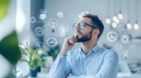 Young bearded businessman in glasses thinking creatively with illustrated light bulbs and innovation icons floating around his head in modern office space.