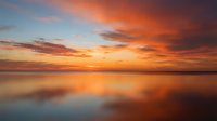 Dramatic sunset over calm water with vibrant orange and pink clouds reflecting on glassy surface, ideal for travel, nature, and inspirational design projects.