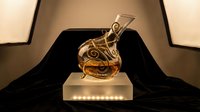 Golden music award trophy with treble clef design on illuminated pedestal against dramatic black velvet backdrop for ceremonies and recognition events.